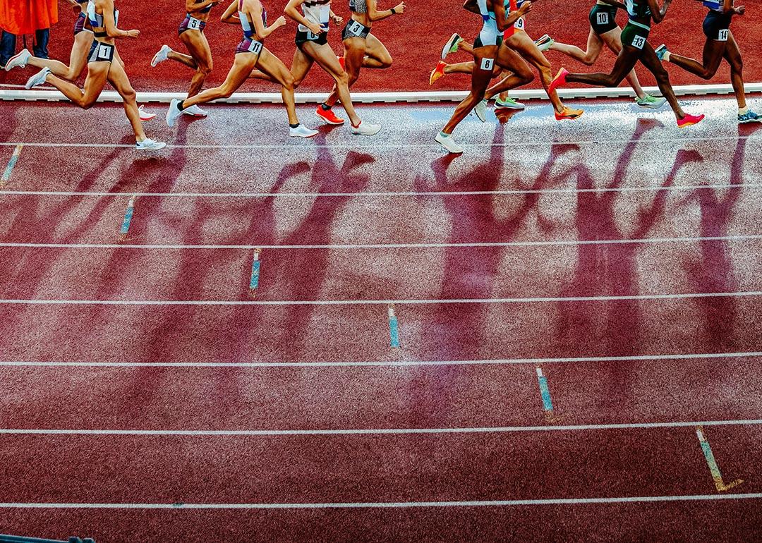 Legs of female track and field athletes running on the track cast long shadows onto the red track during professional 1500 m race.