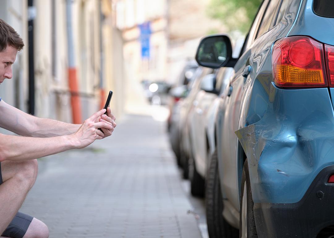 A man taking a photo of his damaged car caused by a hit-and-run.