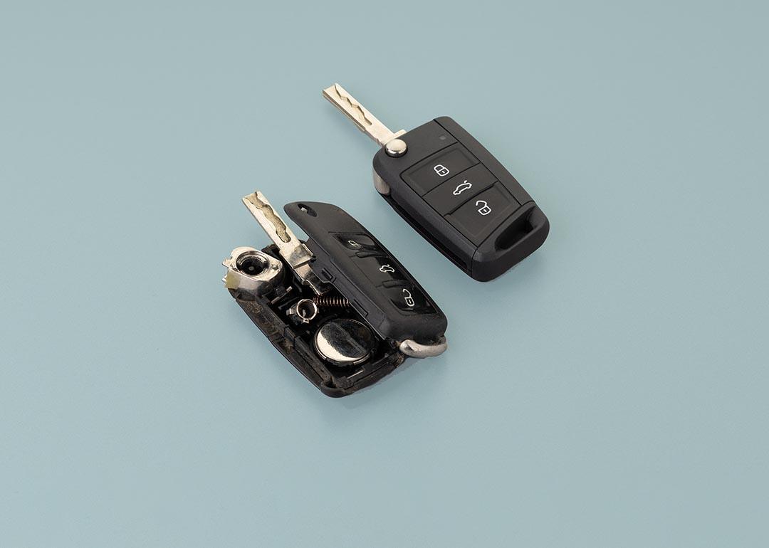 Broken damaged car key gob and new remote vehicle key side by side against pale greenish grey background.  