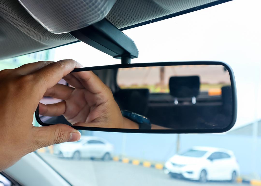 Hand of a driver getting ready for a drive by adjusting rear view mirror of car.