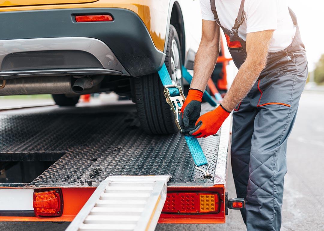 Close up of older man securing a yellow car to a flatbed tow truck with ratchet straps.