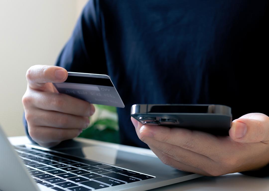 A person holding a credit card, making a purchase payment using a laptop and a phone.