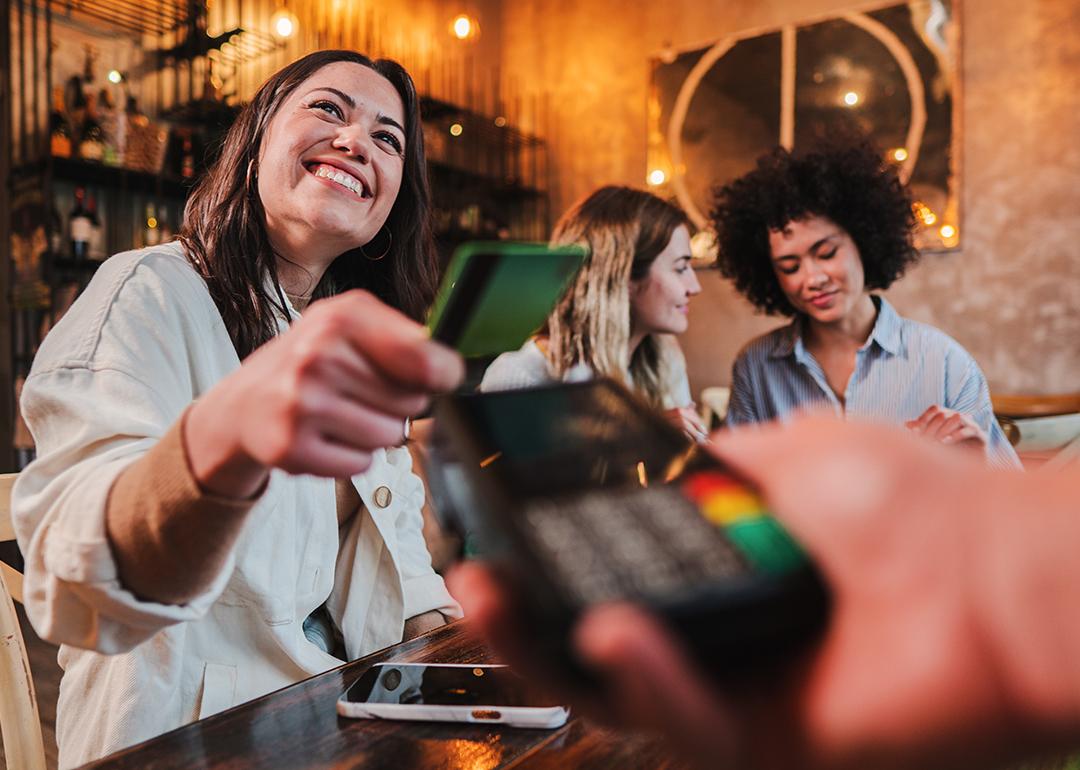 A group of young women dining out and one of them pays with a credit card.