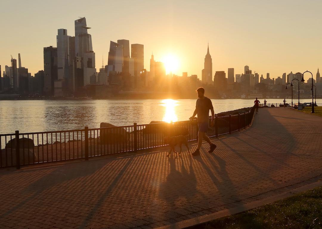 A person walks their dog in Hoboken, New Jersey, along the Hudson River, as the sun rises behind the skyline of Manhattan during a heatwave in September 2023.