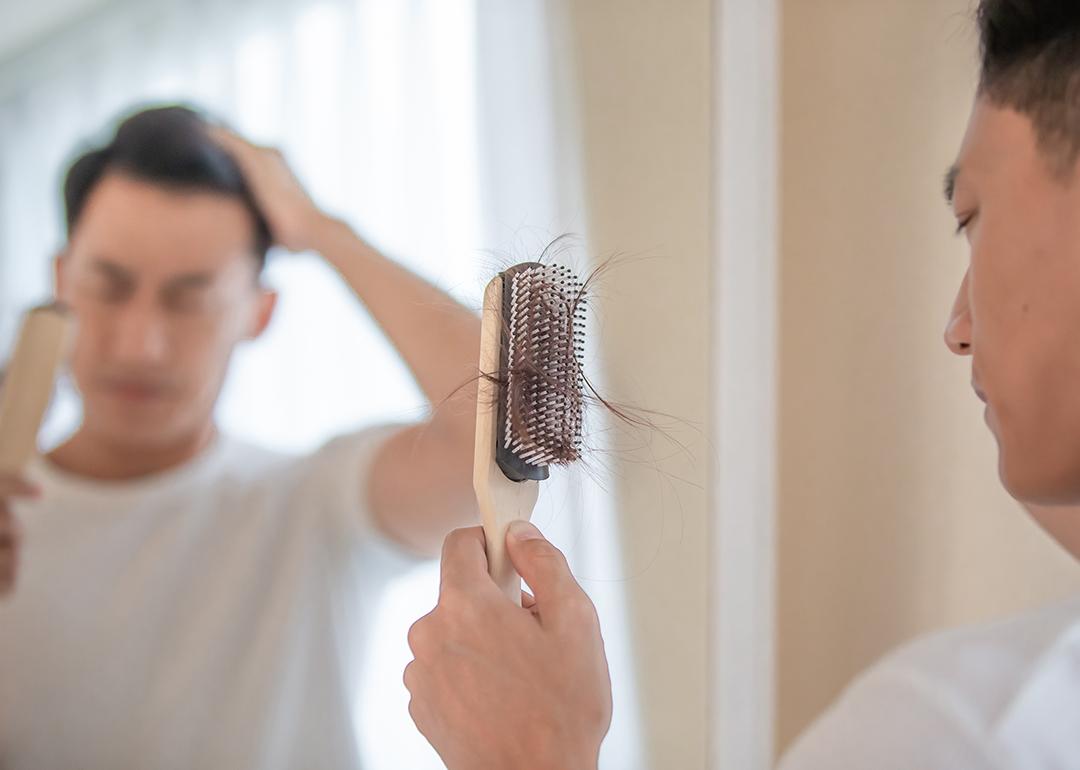 A man looking at his brush with plenty of hair loss.