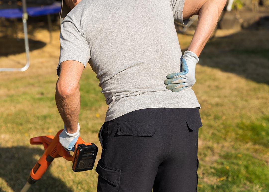 View from behind of person pushing lawn appliance while holding arm to back in pain.