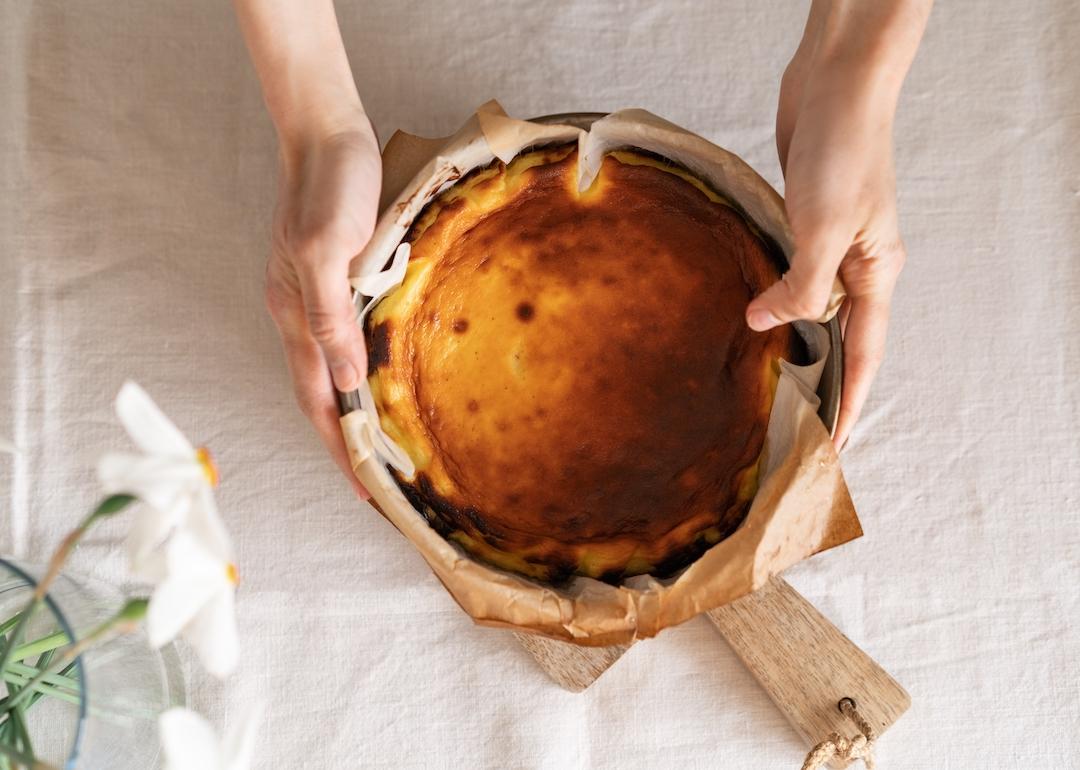 Top view of baker holding basque cheesecake in baking paper.