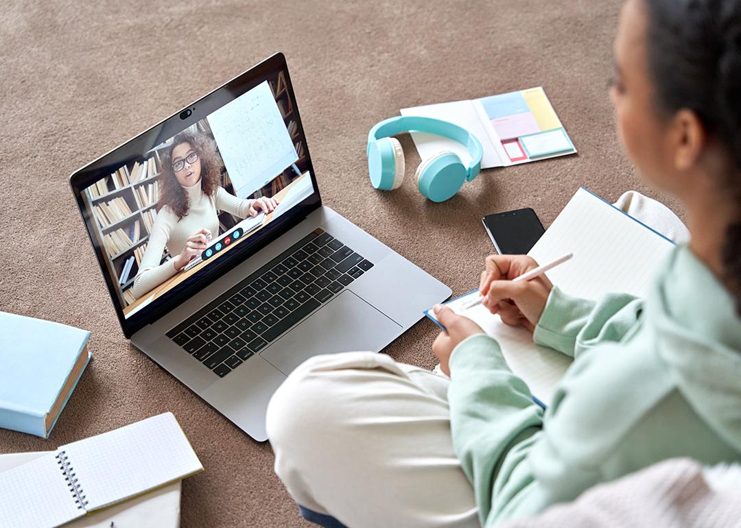 A female college student sitting on the floor while engaging in a virtual class.