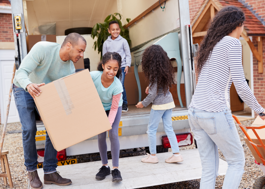 Family unpacks cardboard boxes from moving truck.