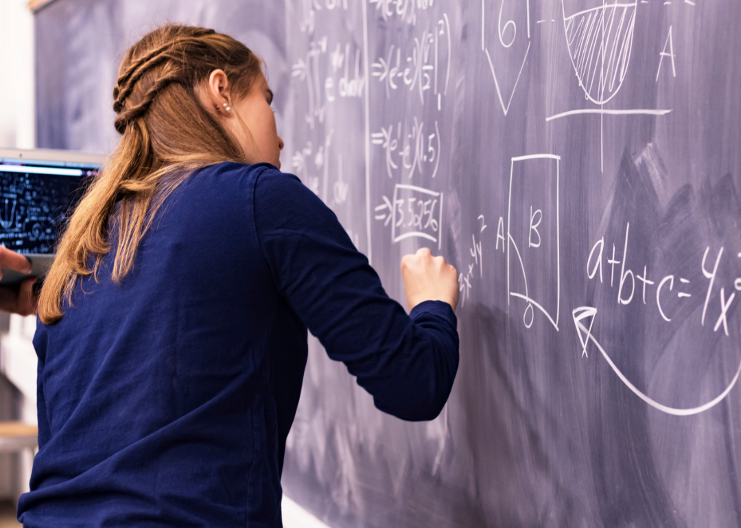 High school student working out a math problem on a classroom chalkboard