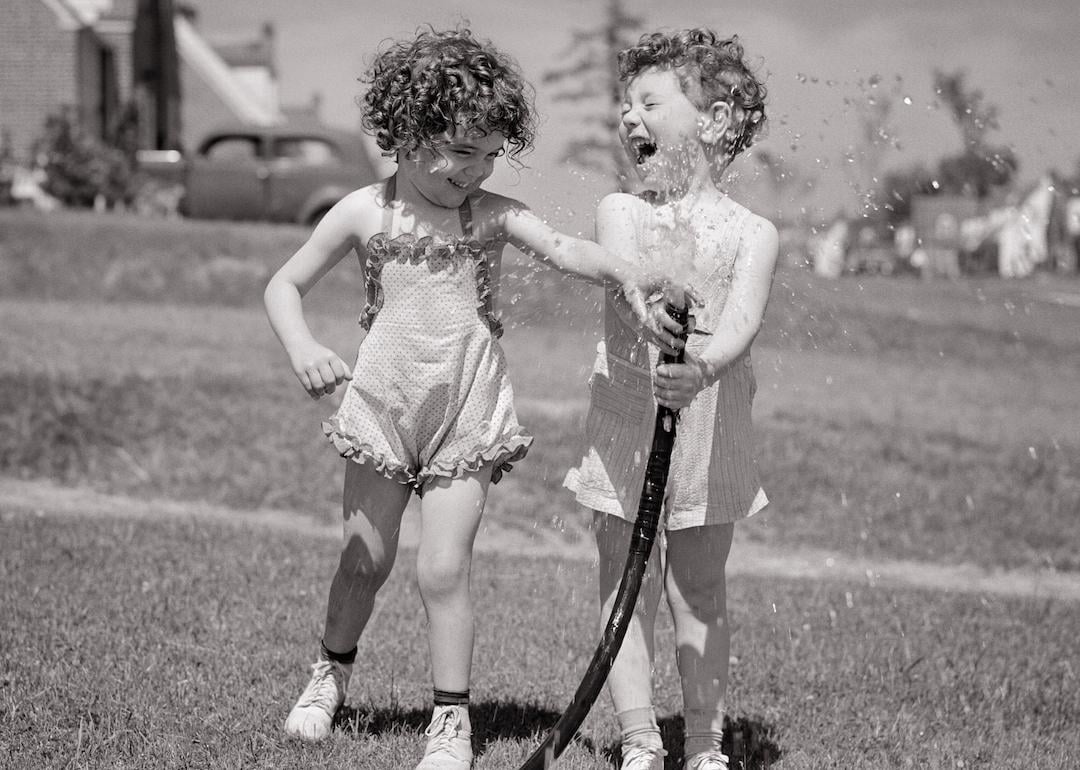 Children in the 1950s splashing water from a garden hose during the summertime.