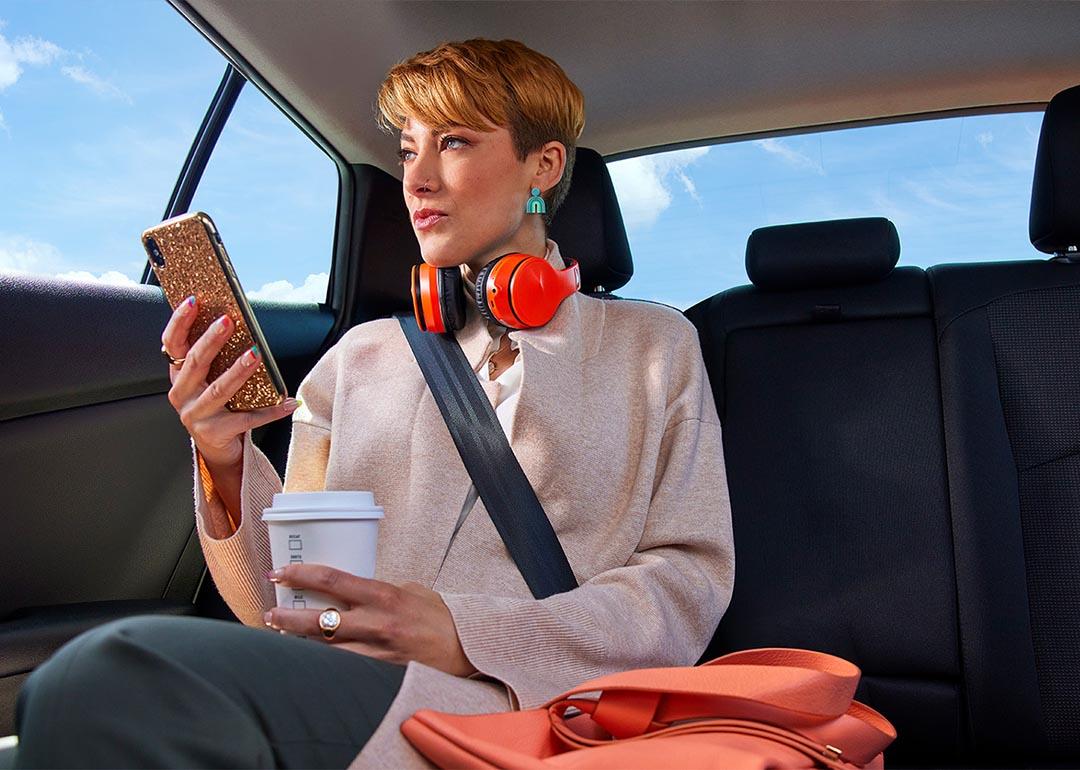 Photo of a commuter looking at a phone from the backseat of a rideshare. 