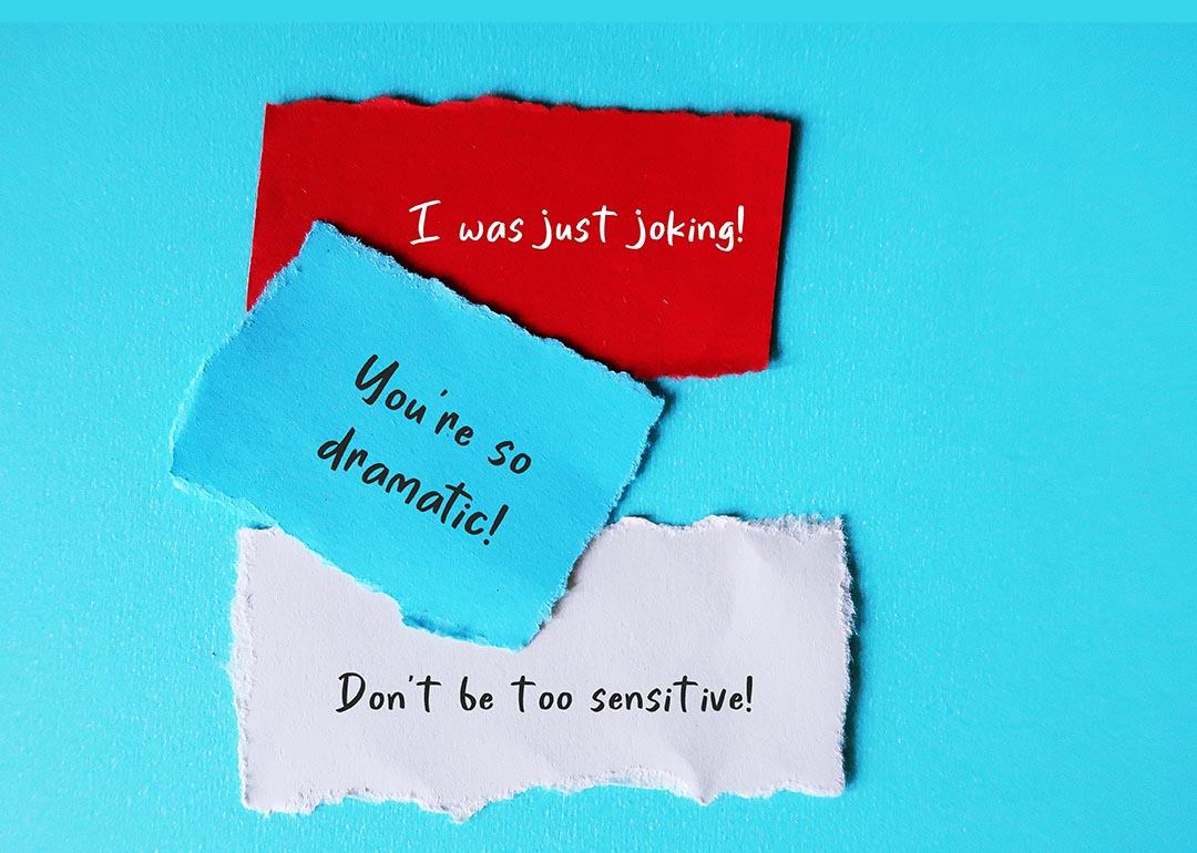 Notes saying "I was just joking," "don't be so dramatic," and "don't be too sensitive!" written on paper and stuck to blue background. 