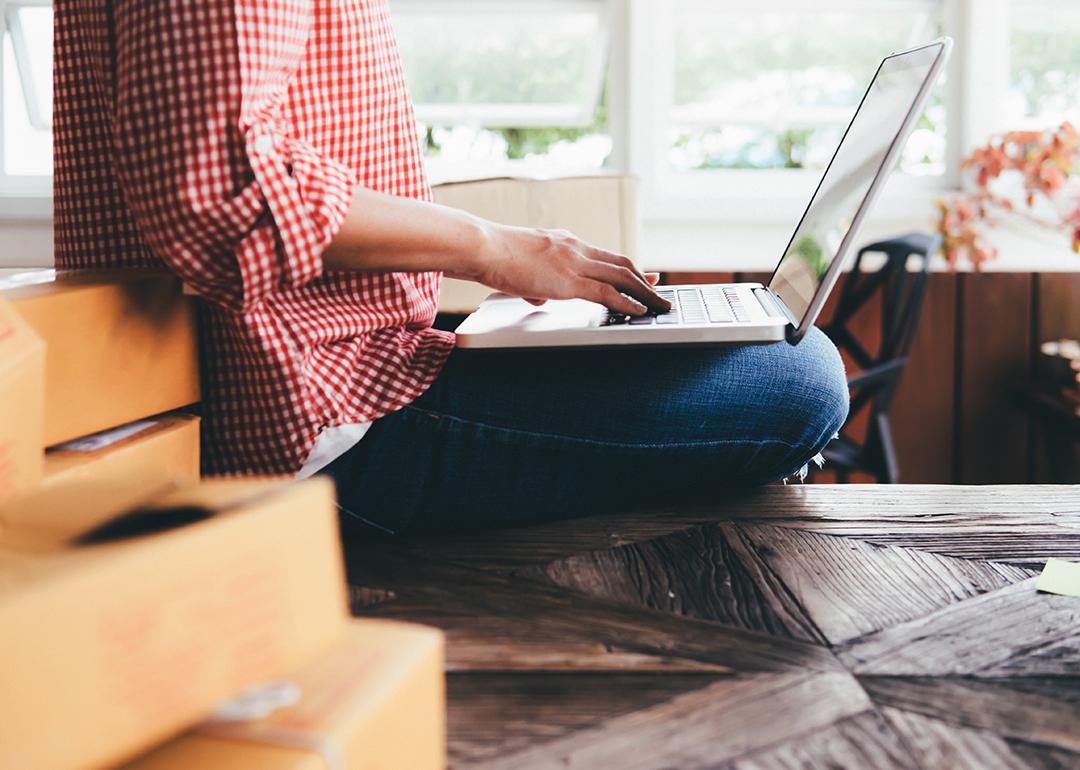 A female small business owner with boxes behind her using a laptop.