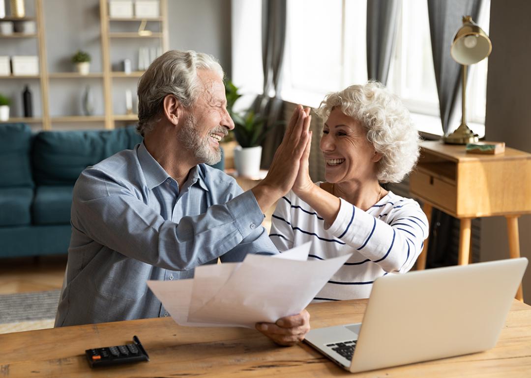 A baby boomer couple giving each other high five while doing finances.