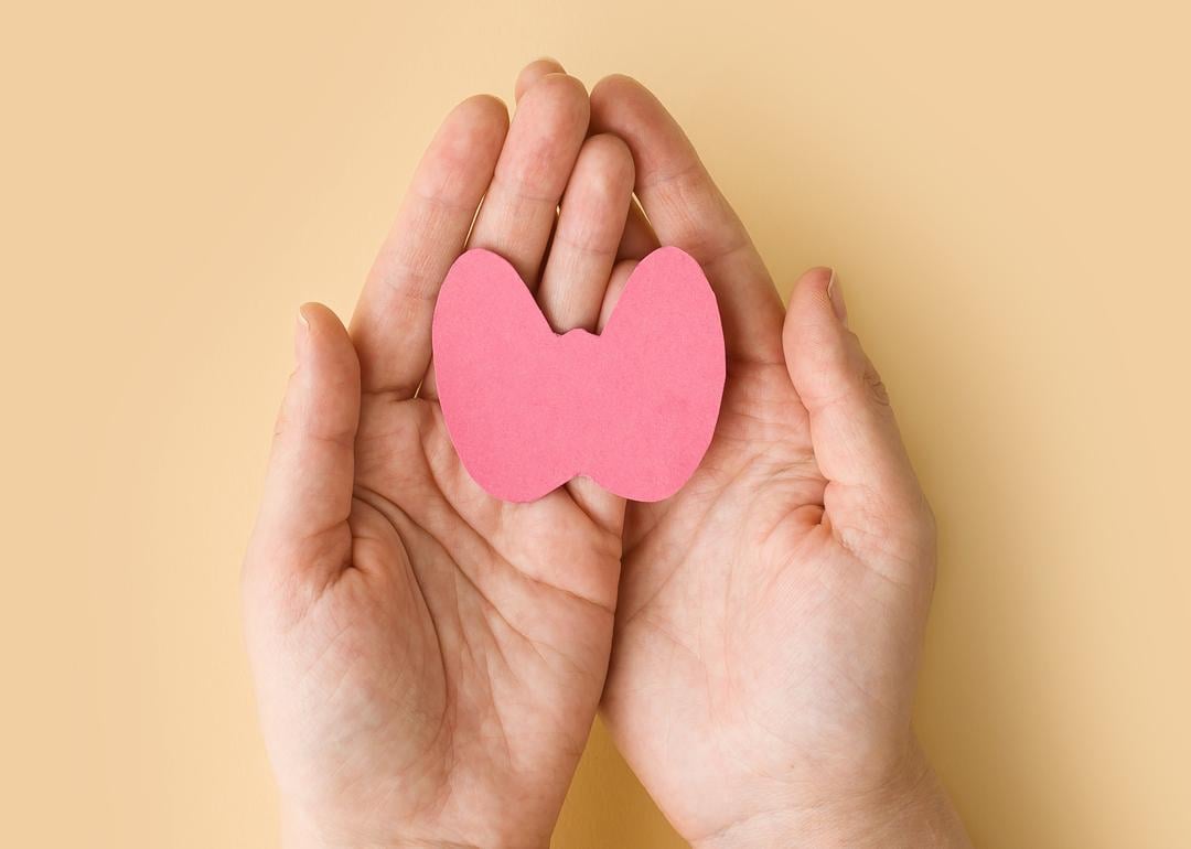 A woman's hands holding a paper form of the thyroid gland on a beige background.