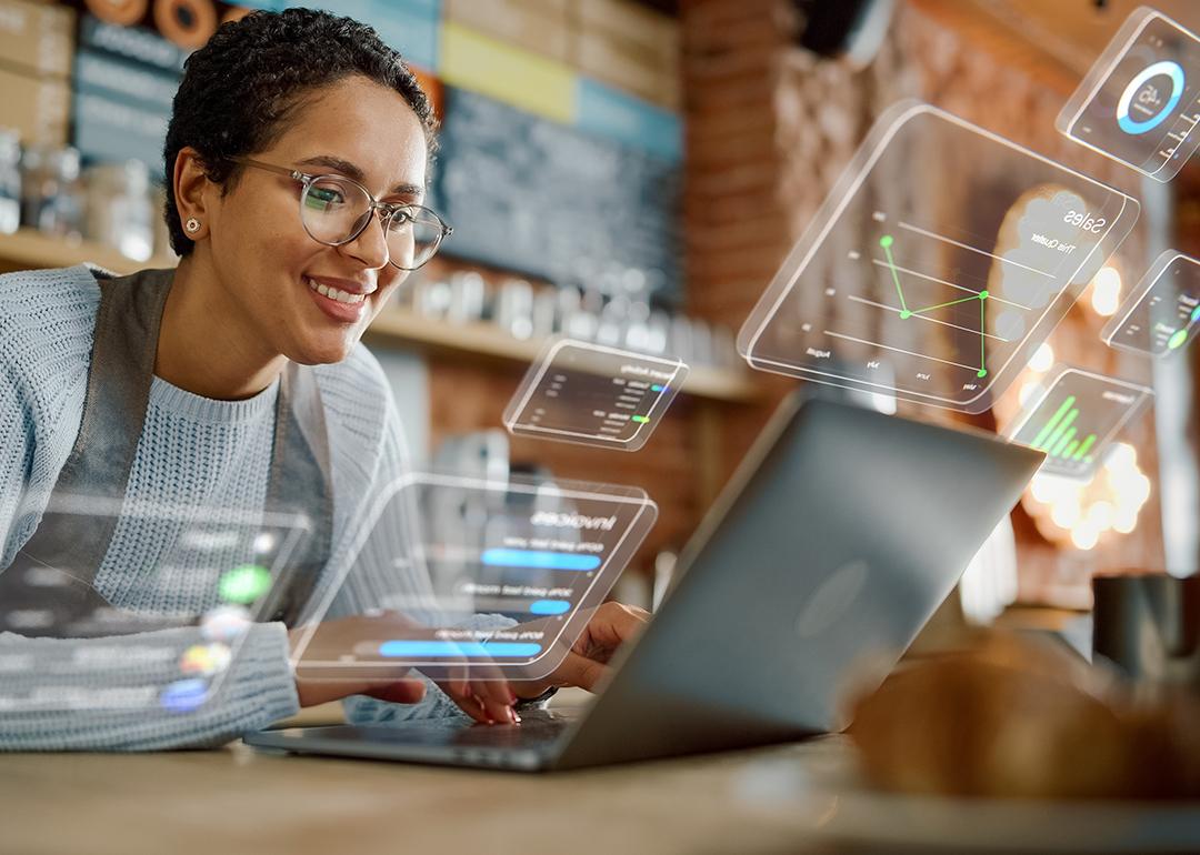 A female business owner using a laptop and illustrated with different holographic icons representing apps.