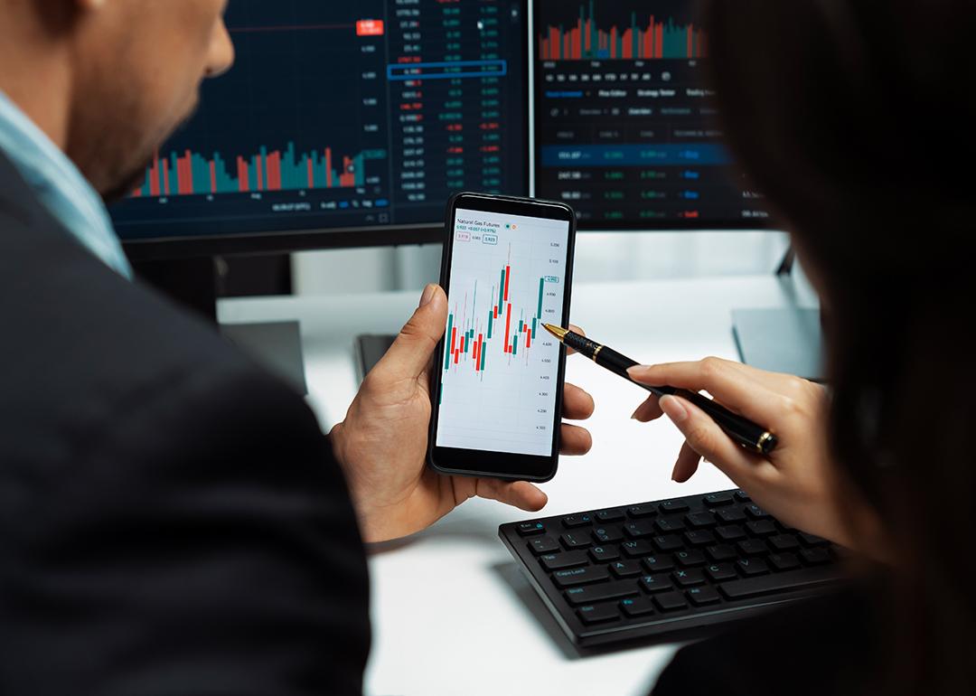 Two finance professionals looking at a smartphone monitoring stock and trade news.