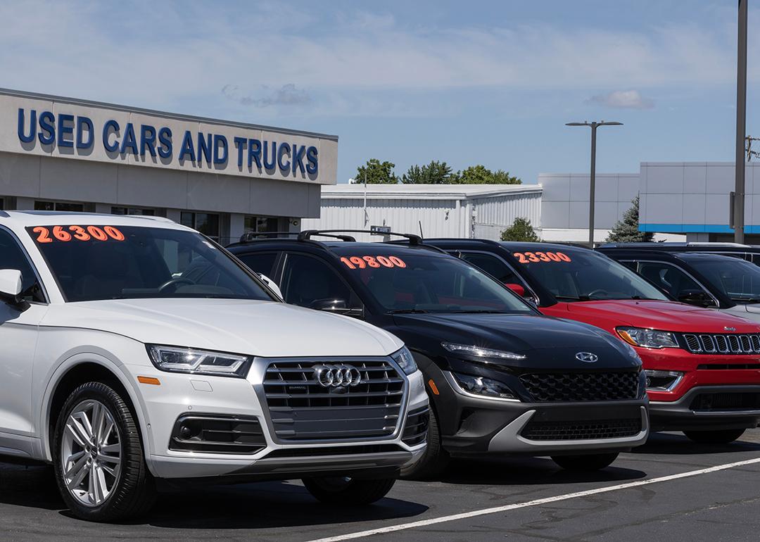 A row of cars in a dealership lot with a signage saying "used cars and trucks" in the background.