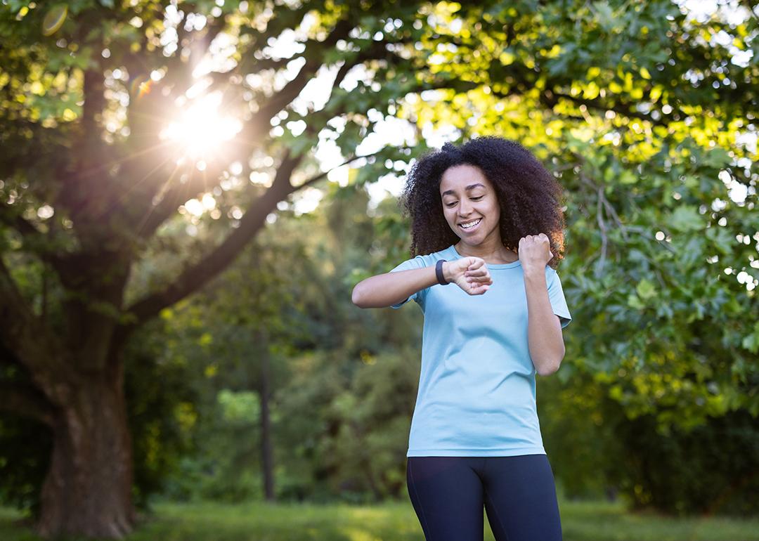 A young lady exercising outdoors is looking at her fitness tracker watch.