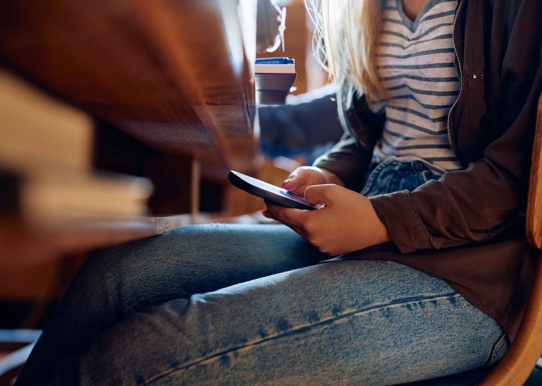 Young student using cell phone under a desk during class.