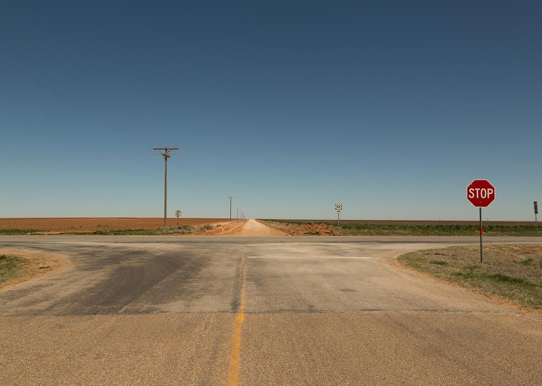 A rural intersection in Texas with a stop sign and a blue sky in the background.