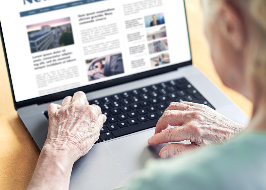 View of older person from behind looking at news website on laptop computer.