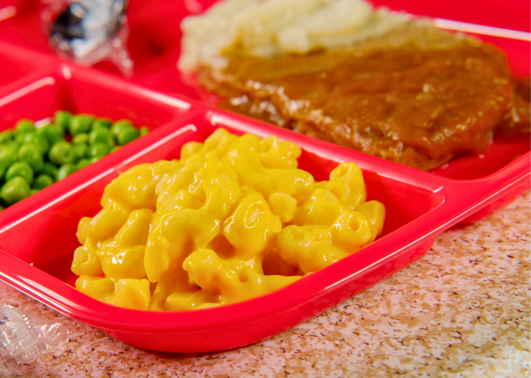 TV dinner with Salisbury steak, macaroni and cheese, and peas on a red tray.