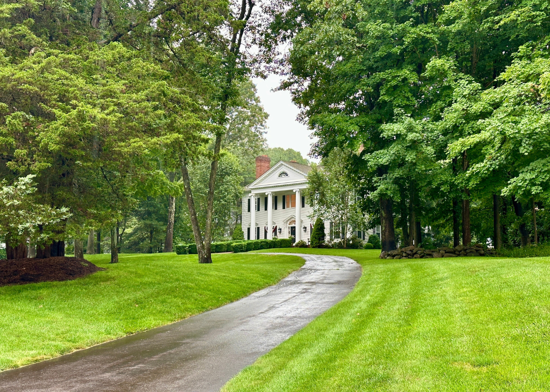 A colonial-style white house at the end of a long driveway in an affluent neighborhood in Madison, Connecticut