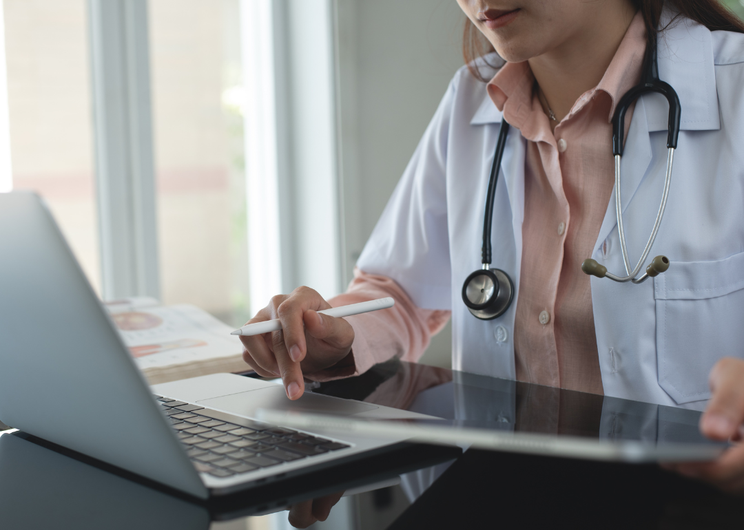 A doctor working on a laptop and using a digital tablet.