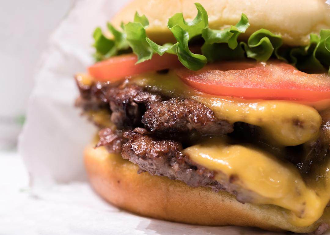 Double cheeseburger in a wrapper with tomato, lettuce, and onion.