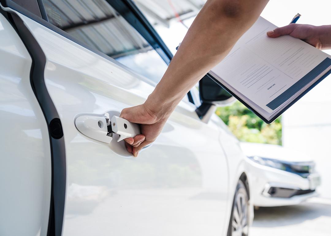 Person inspecting a car while filling out a car insurance form.