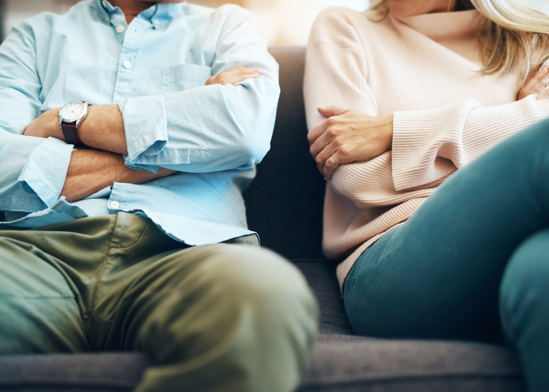 A fighting couple sit apart on a sofa