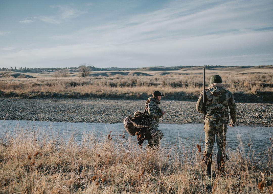 Two people out hunting in a vast field.