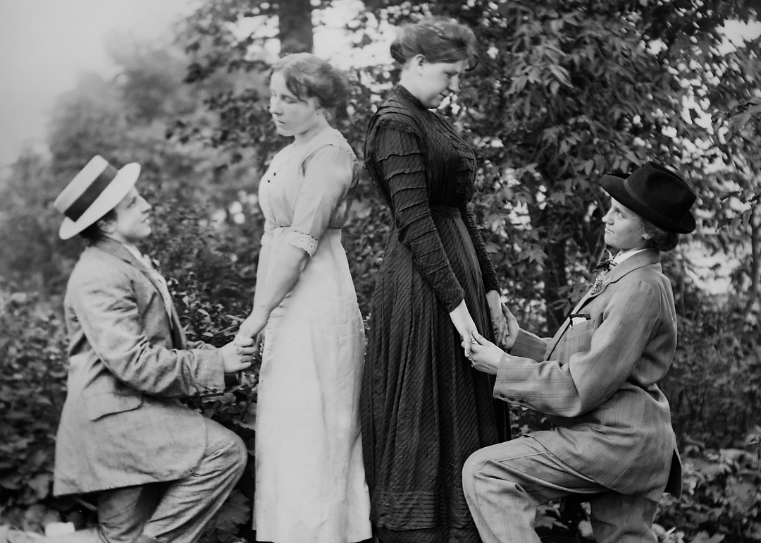 Two women dressed in suits proposing marriage to two women in unison, circa 1910. 