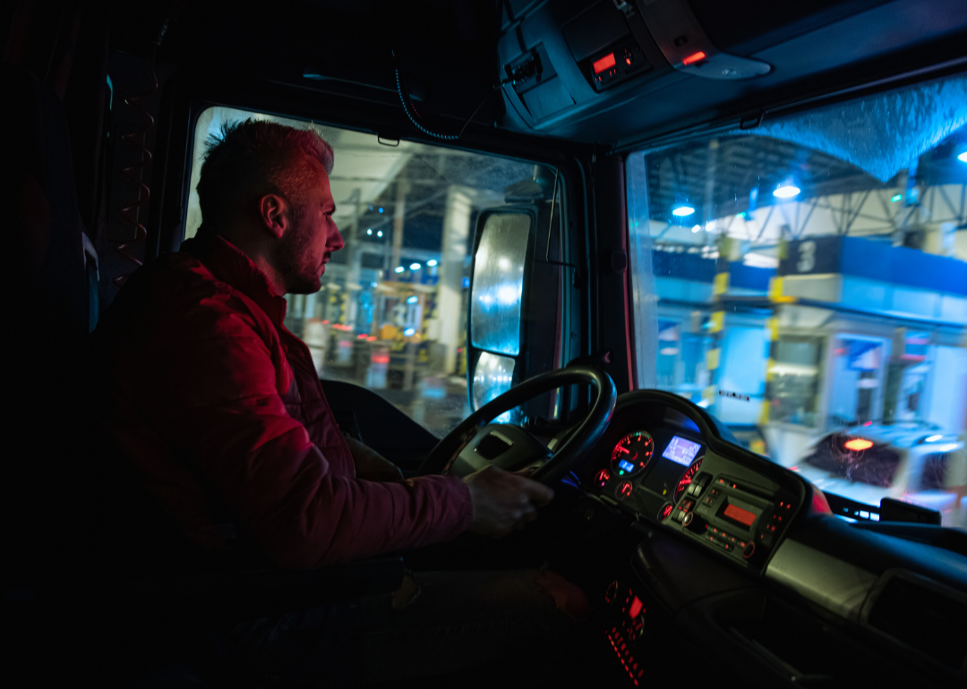 A driver steers behind the wheel of a truck at night.