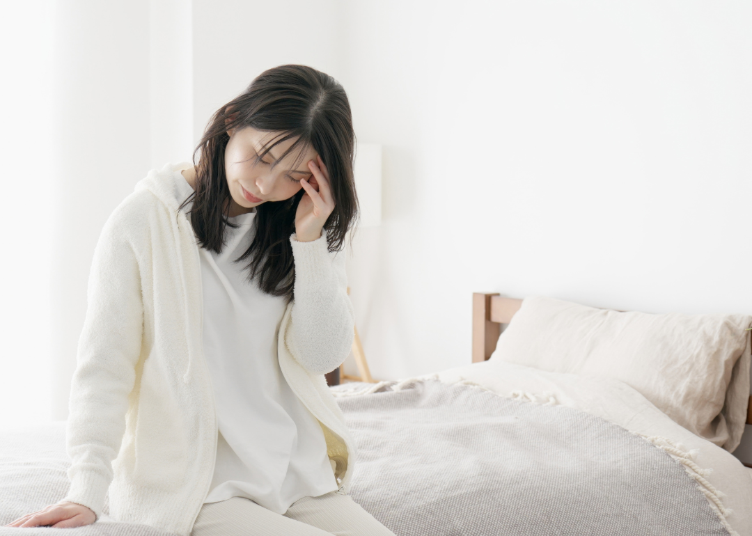 Unwell woman sitting on the edge of a bed with a hand on her forehead