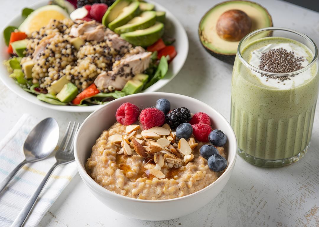 Healthy meals such as oatmeal with berries, quinoa with chicken and a glass of avocado smoothie on a table..