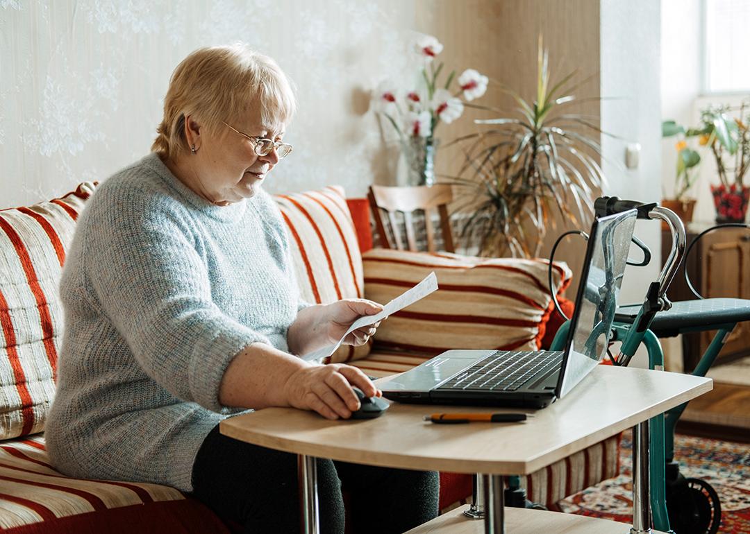 An older woman with disability looking up insurance information online using a laptop.