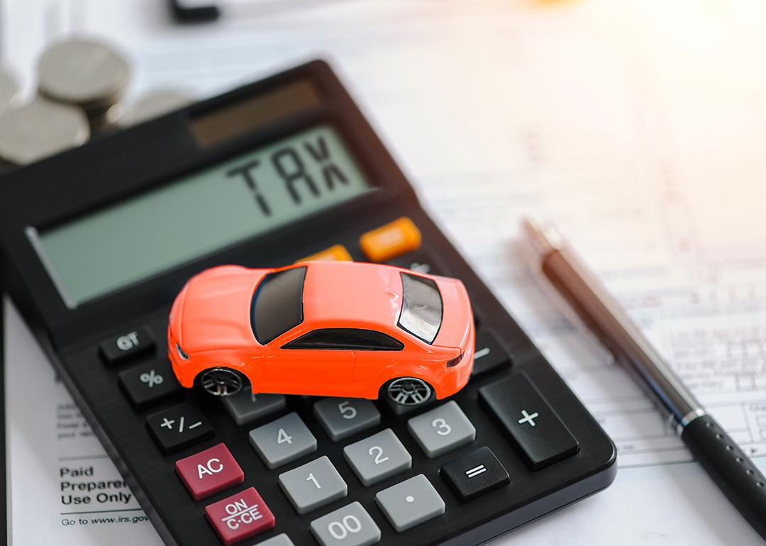 A miniature car figure on top of documents and a calculator indicating 'tax'.