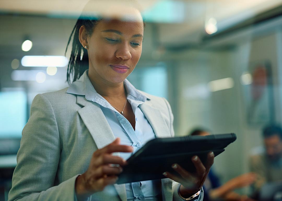 African American female consultant using touchpad while her clients are in the background in the office. 