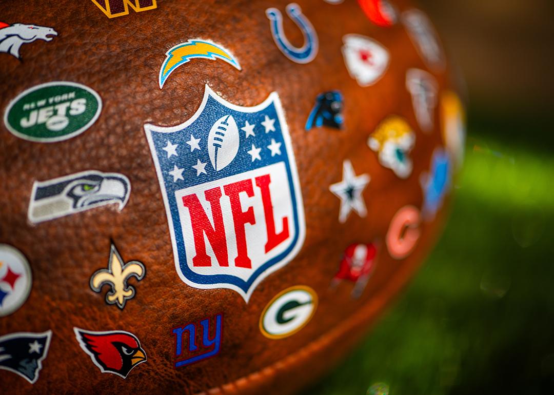 A focus shot on an NFL game ball featuring all logos of NFL teams.