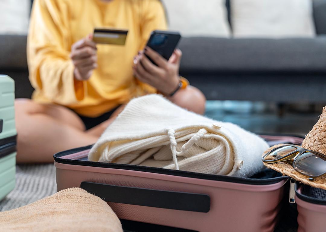 A woman planning a trip using credit card and phone while preparing a suitcase.