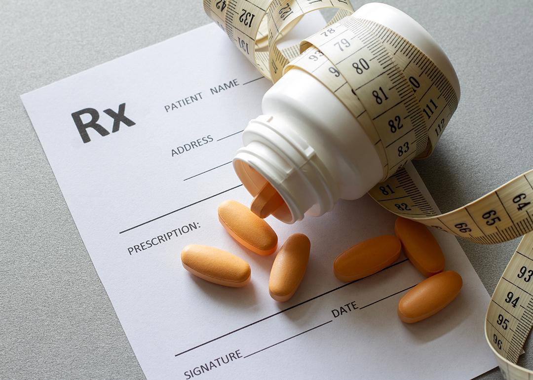 Bottle of pills wrapped with a tape measure on top of a prescription.