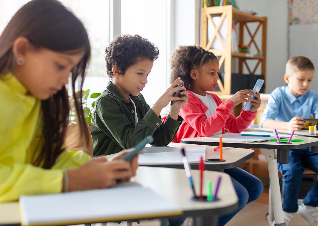 Diverse group of schoolkids using smartphones in classroom.