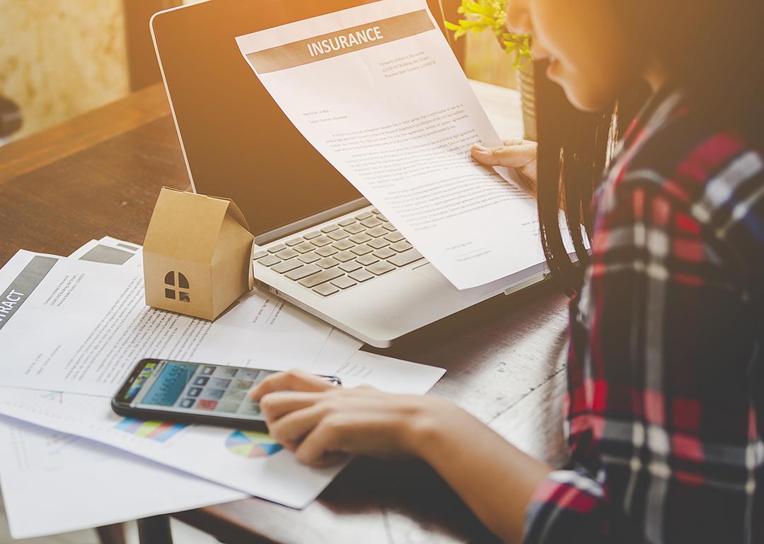 A young woman looking up information on home contracts and insurance using a phone and a laptop.