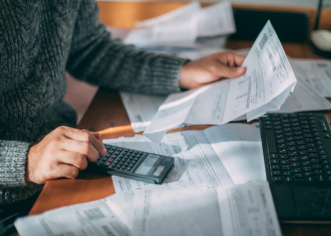 Person holding loan and utility bills while using a calculator.