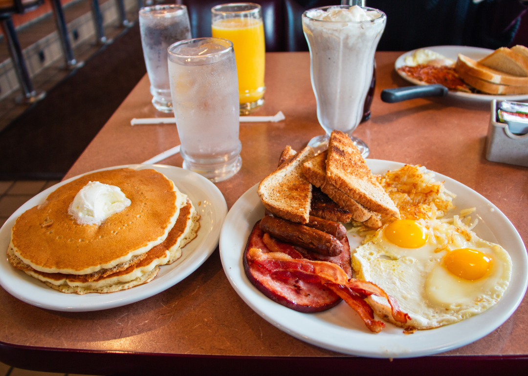 Plates of pancakes and fried eggs, bacon, sausages and toast on a diner table