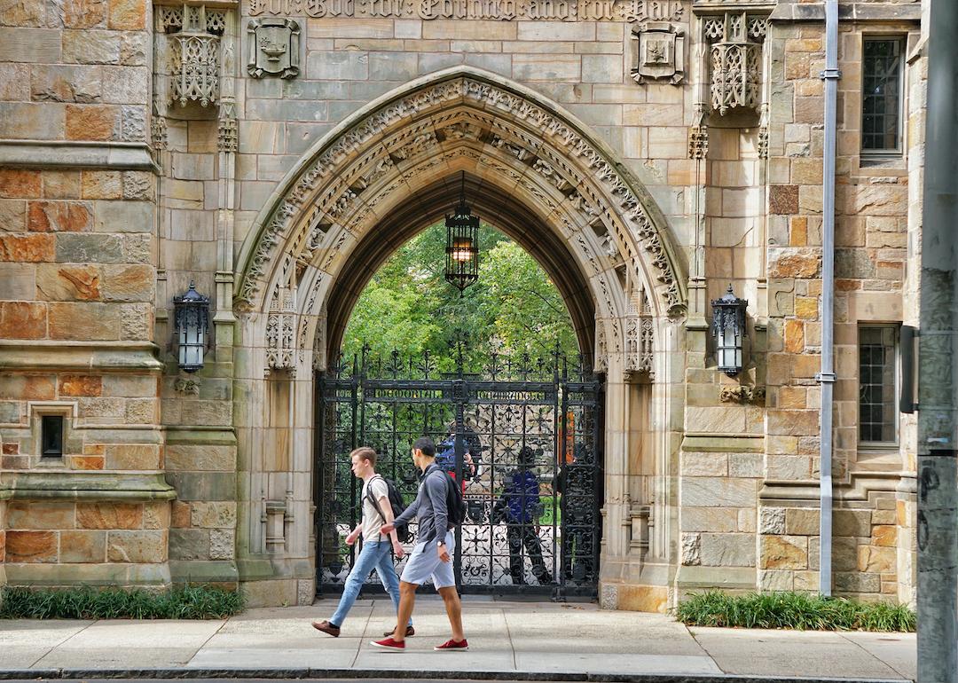 Students walk past a decorative stone archway at the entrance to Yale University in New Haven, Connecticut.