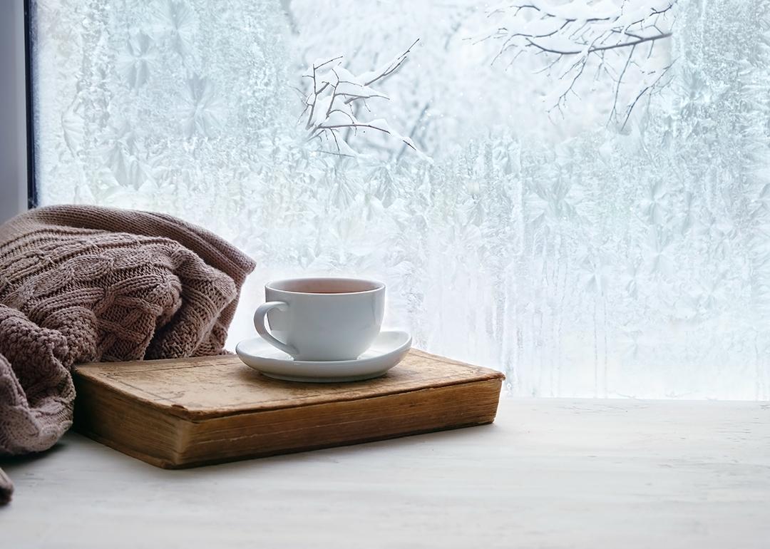 A cup of coffee on a home window showing peak winter season.